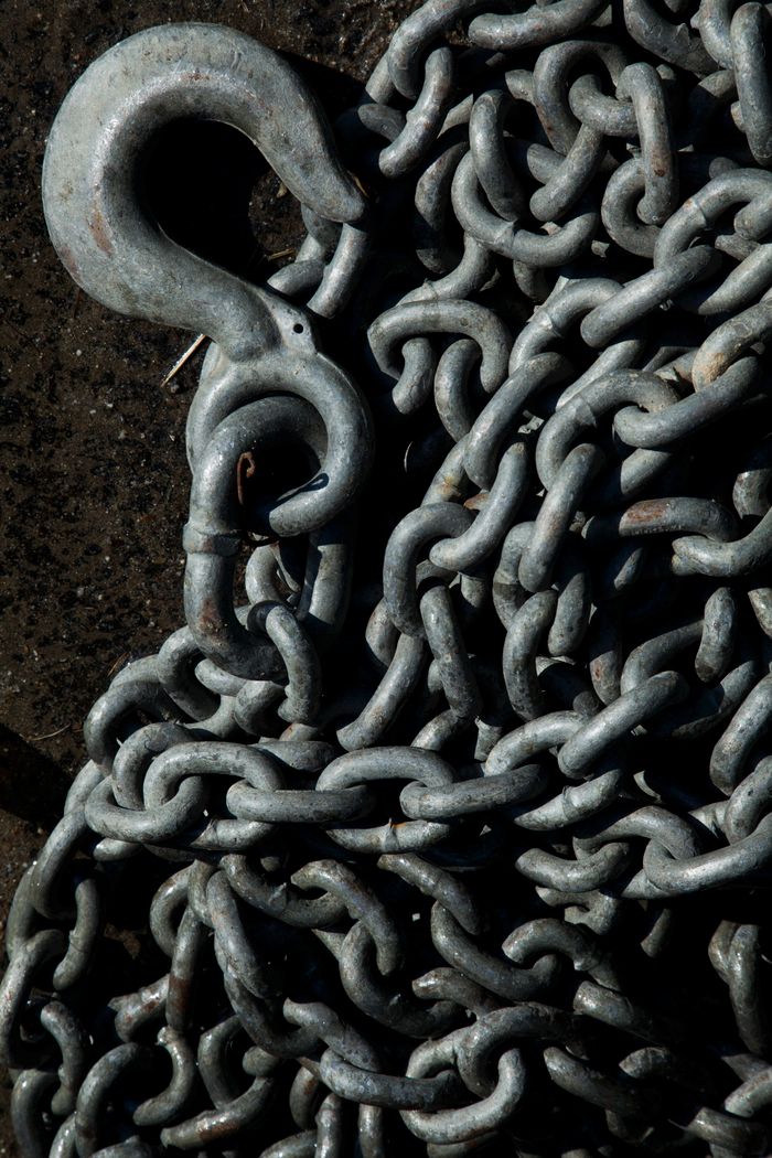 Detailed shot of an intertwined iron chain with a large metal hook, perfect for industrial or nautical themes.